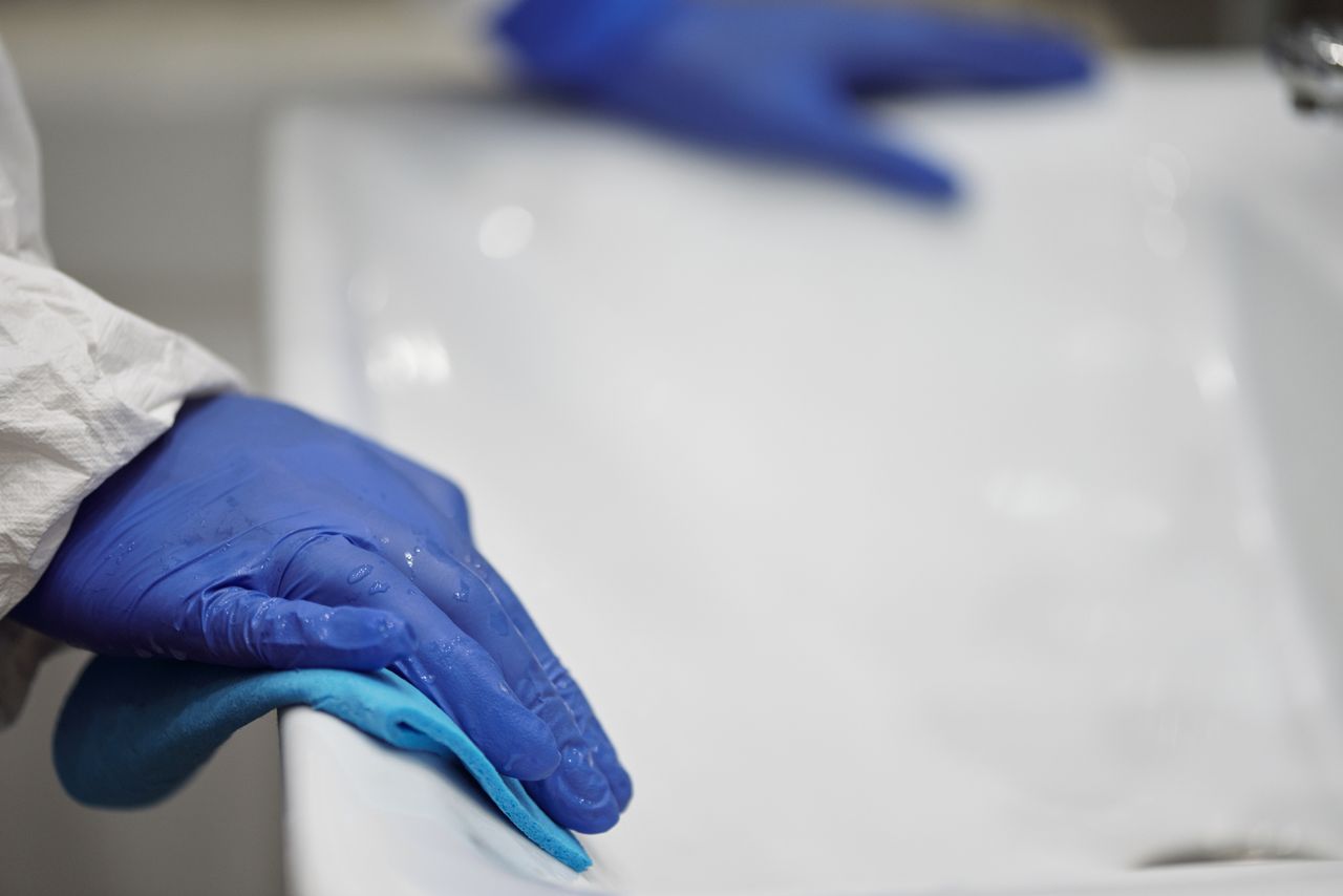 Gros plan sur une personne désinfectant un lavabo de salle de bain avec des gants et un chiffon, mettant l’accent sur l’hygiène et la propreté.